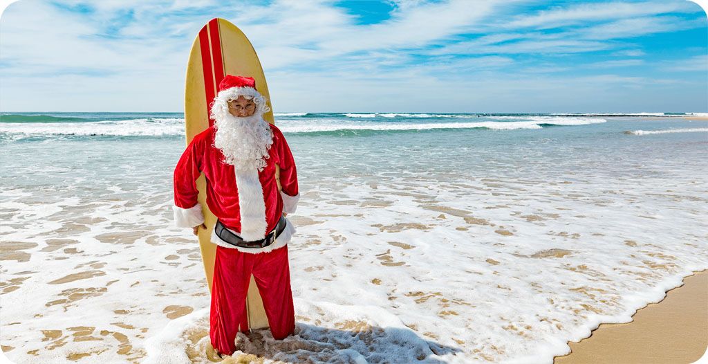 Person dressed as Santa standing with a surfboard